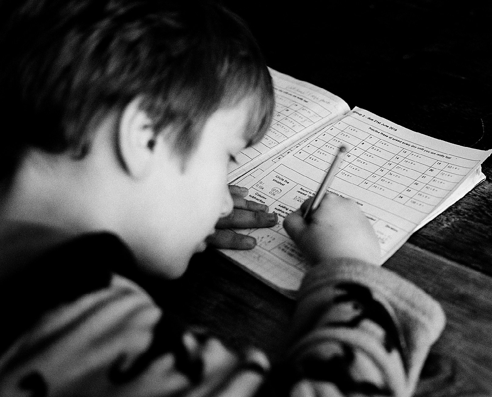 A young student working through a page of maths problems at a desk.